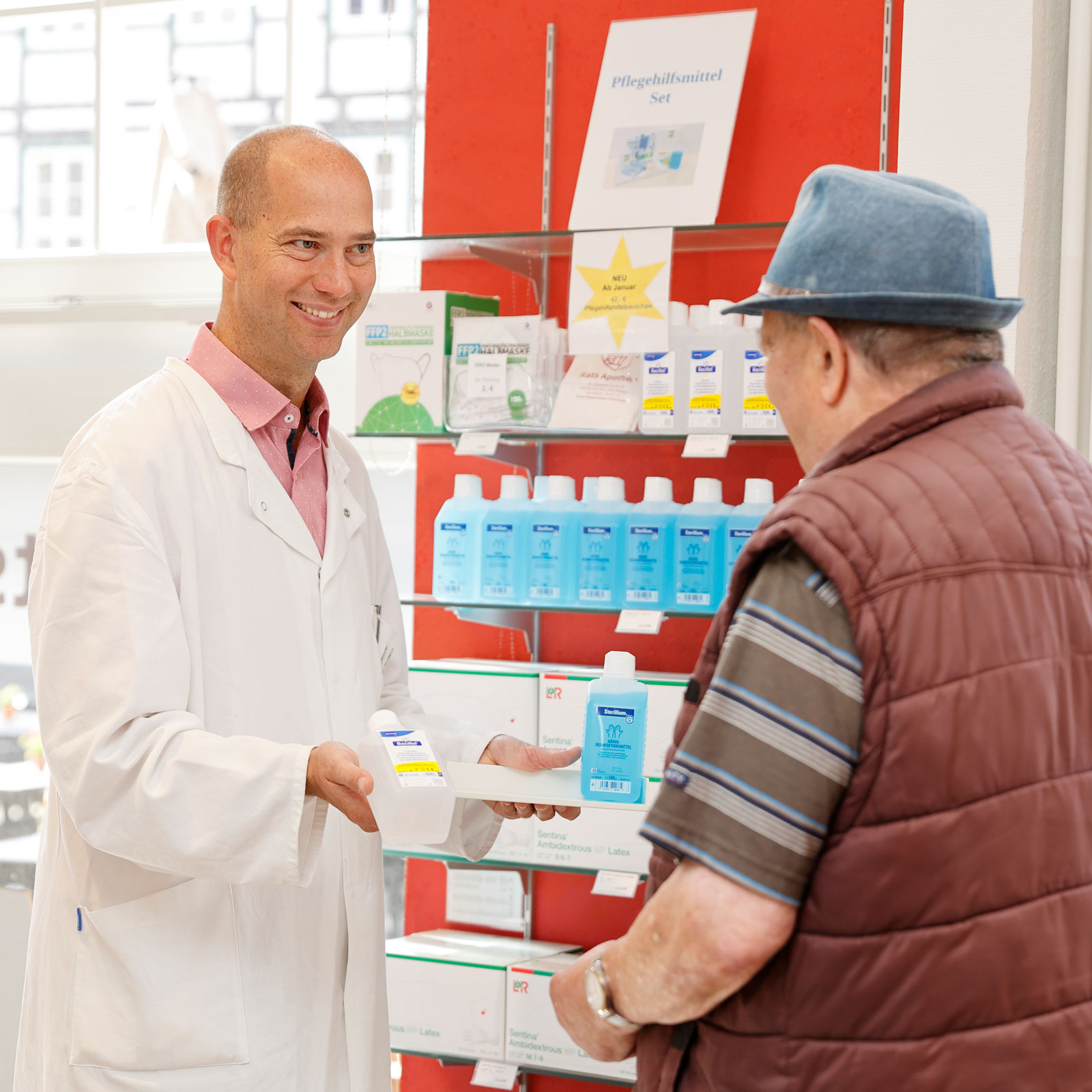 Apothekenmitarbeiter berät einen älteren Mann zu Hilfsmitteln.